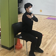 검사자가 의자에 앉아서 양팔을 십자모양으로 교차하여 가슴 앞에 모으고 두손은 어깨 위에 올리고 있다